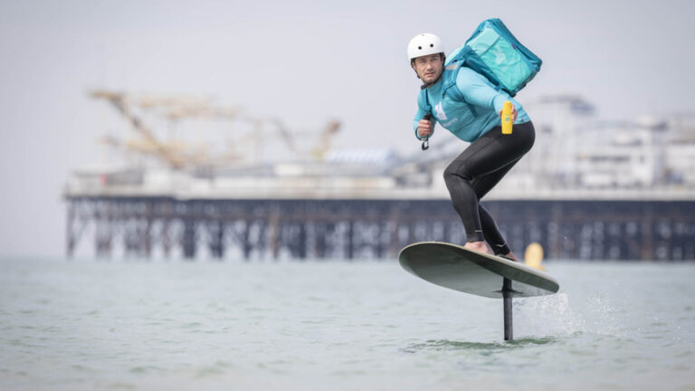 Deliveroo entrega protetor solar na praia em cima de prancha de surfe