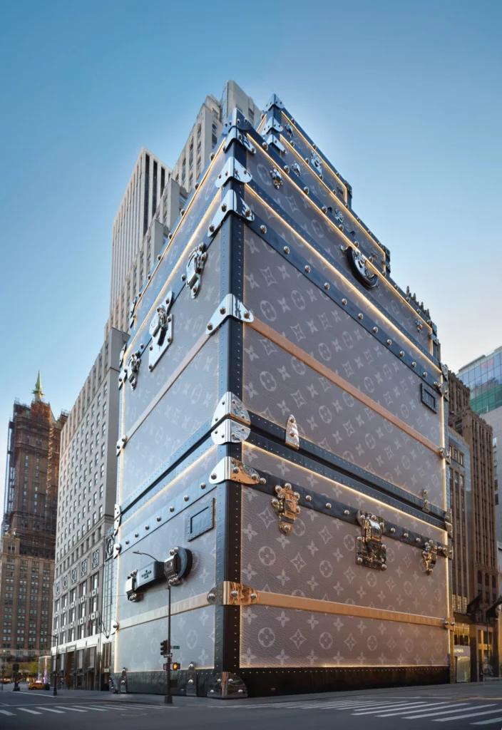 A Louis Vuitton, ícone mundial da moda de luxo, surpreendeu mais uma vez ao cobrir sua icônica flagship store na Quinta Avenida, em Nova York, com uma instalação artística de tirar o fôlego. A marca cobriu completamente o edifício, que está em reforma por três anos, com uma fachada que simula seis baús gigantes empilhados, uma referência direta aos seus famosos baús de viagem.